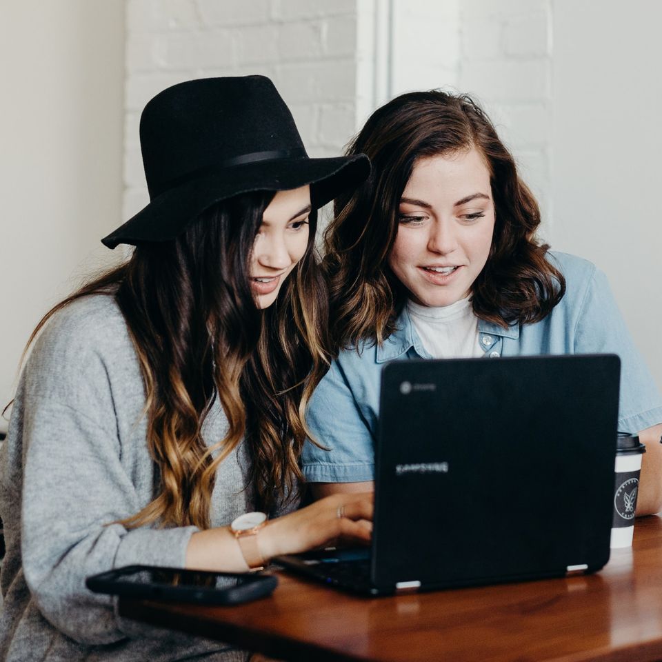 Investieren und Geldanlage lernen auf Finanzwissen.de | © Unsplash/Brooke Cagle Zwei junge Frauen sitzen am Laptop und diskutieren über einen Artikel | © Unsplash/Brooke Cagle